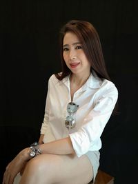 Portrait of smiling beautiful woman sitting against black background