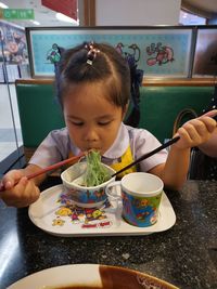 Cute girl eating food on table in restaurant