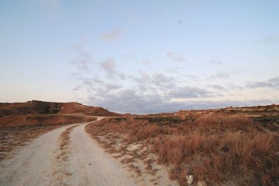 Dirt road amidst field against sky