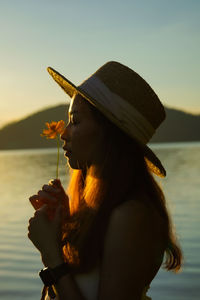 Side view of woman by lake against sky during sunset