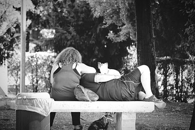 Rear view of woman sitting on tree trunk