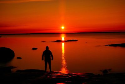 Silhouette people standing on beach against orange sky