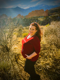 Portrait of smiling pregnant woman standing on field against sky