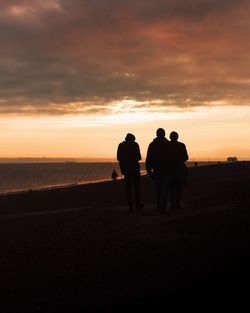 Silhouette men on beach against sky during sunset