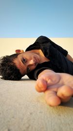 Portrait of young man lying down on land against clear sky
