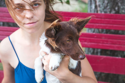 A girl in a blue sundress sits on a bench and holds a little brown and white dog. love pets, dog day