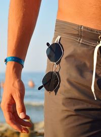 Midsection of man with sunglasses at beach