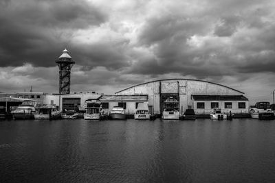 Sailboats in river by buildings against sky