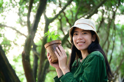 Portrait of smiling young woman holding plant in forest