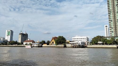 Buildings at waterfront against cloudy sky