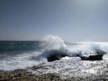 Waves splashing on rocks against clear sky