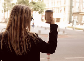 Rear view of woman holding coffee in city