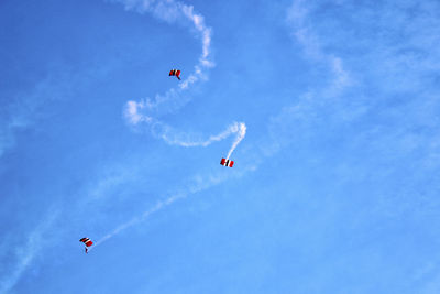 Low angle view of parachutes flying against blue sky
