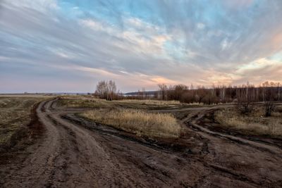 Dirt road amidst field against sky