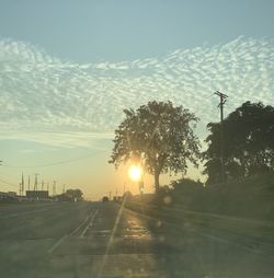 Road by trees against sky during sunset