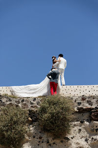 Man and woman standing on wall against clear blue sky