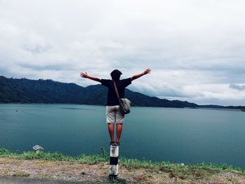 Woman with arms outstretched standing at lakeshore