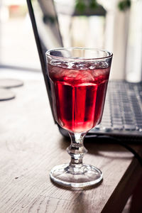 Close-up of red drink in glass by laptop on table 