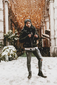 Full length portrait of man standing in snow against illuminated lighting equipment outdoors