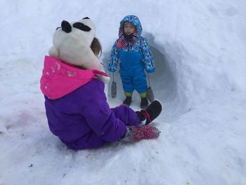 Rear view of siblings by cave in snow covered field