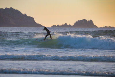 Man surfing in sea against sky during sunset