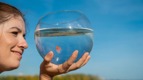 Woman holding round aquarium with goldfish on blue sky background