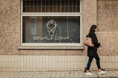 Full length of woman standing on footpath against building