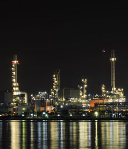 Illuminated buildings by river against sky at night