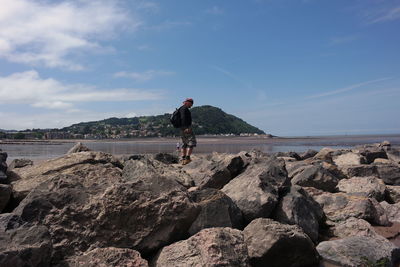 Man on rocks by sea against sky