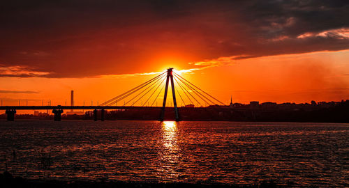 Silhouette bridge over sea against orange sky