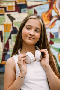 Teen girl with headphones posing on colorful city graffiti background