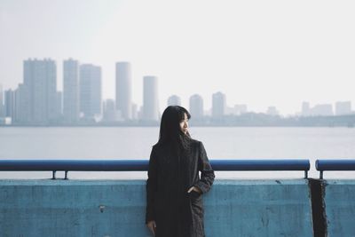 Rear view of woman standing by railing against cityscape