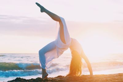 Woman dancing on beach against sky during sunset