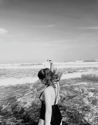 Rear view of young woman standing at beach against sky