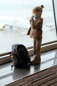 Child with backpack looking though airport window at the airplane. safe travels with kids during