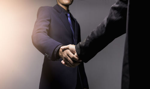 Midsection of businessmen shaking hands on gray background