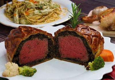 High angle beef wellington cooking cut into slices on the white plate.