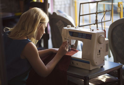 Side view of female fashion designer using sewing machine in studio