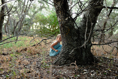 Portrait of girl crouching by tree trunk in forest