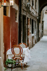 Empty chairs and tables in alley amidst buildings