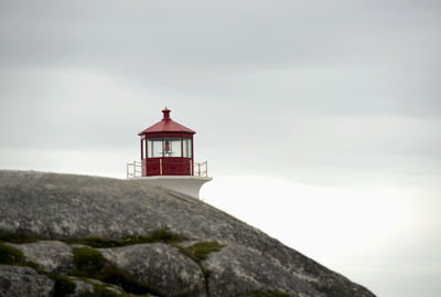 Lighthouse in front of rock against sky