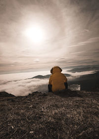 Rear view of man sitting on field against sky during sunset