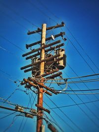 Low angle view of electricity pylon against blue sky