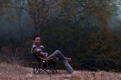 Portrait of young man sitting on chair in forest
