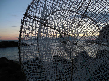 Close-up of fishing net on sea against sky during sunset