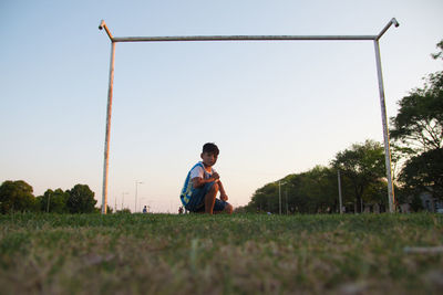 Full length of man sitting on field against clear sky