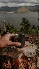 Close-up of hand holding drink by lake