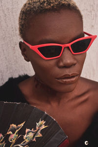 Close-up of woman wearing sunglasses against wall