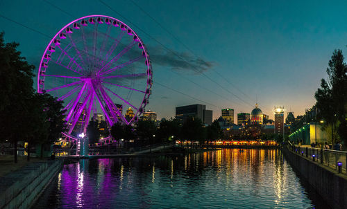 Illuminated ferris wheel by river against sky at night