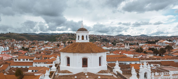 Church amidst buildings against cloudy sky in city